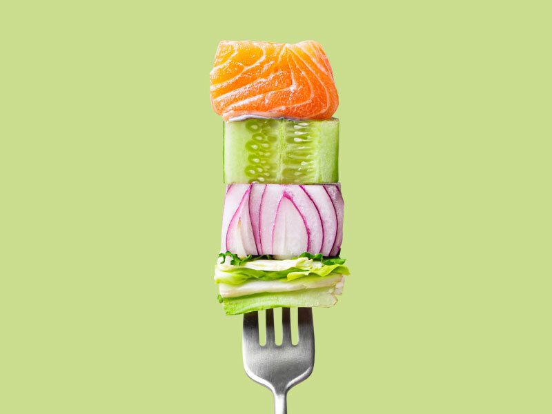 a fork spearing raw salmon and veggies against a green background