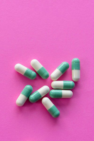 A group of white and green pills on a fuscia surface