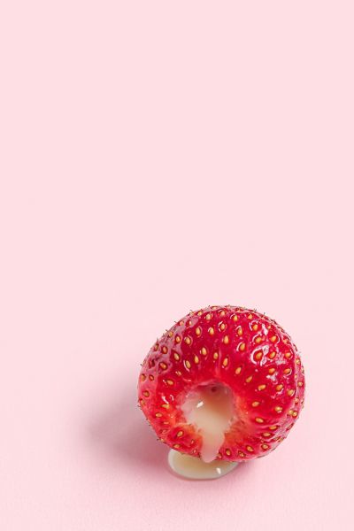 a raspberry oozing a creamy filling on a pink background