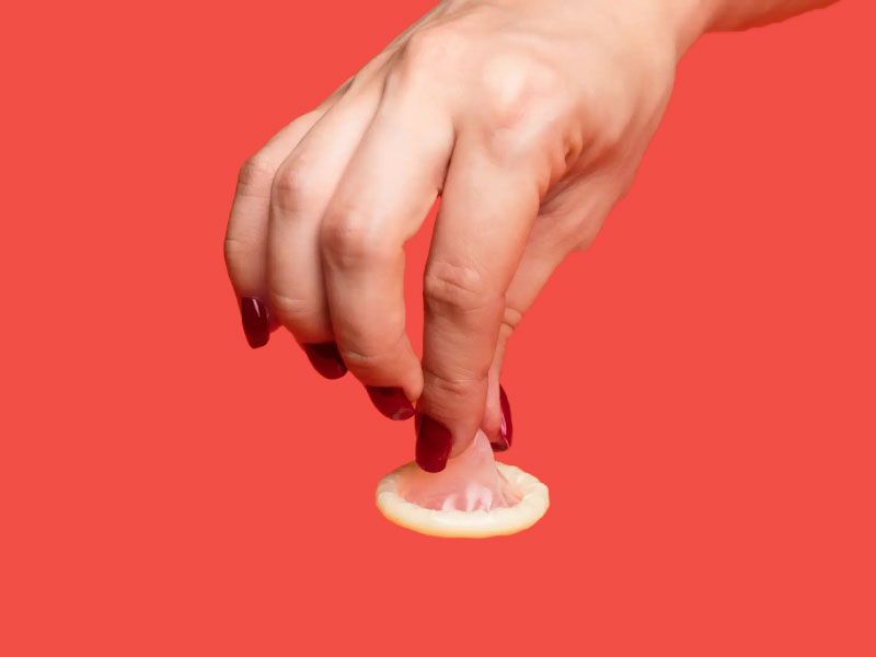 Person's hand holding a condom with a red background
