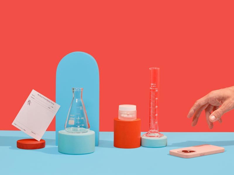 A small Wisp glass jar, test tubes, and rx script and a person's hand reaching for a mobile phone with colorful abstract shapes
