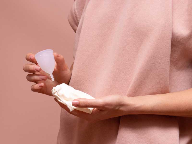 A woman wearing a sweatshirt and holding a menstrual cup