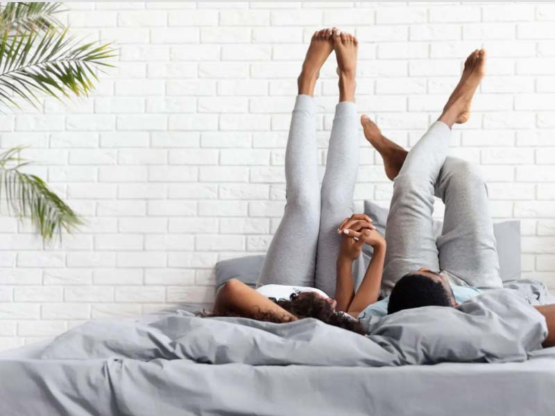 A couple laying in bed holding hands with their feet in the air