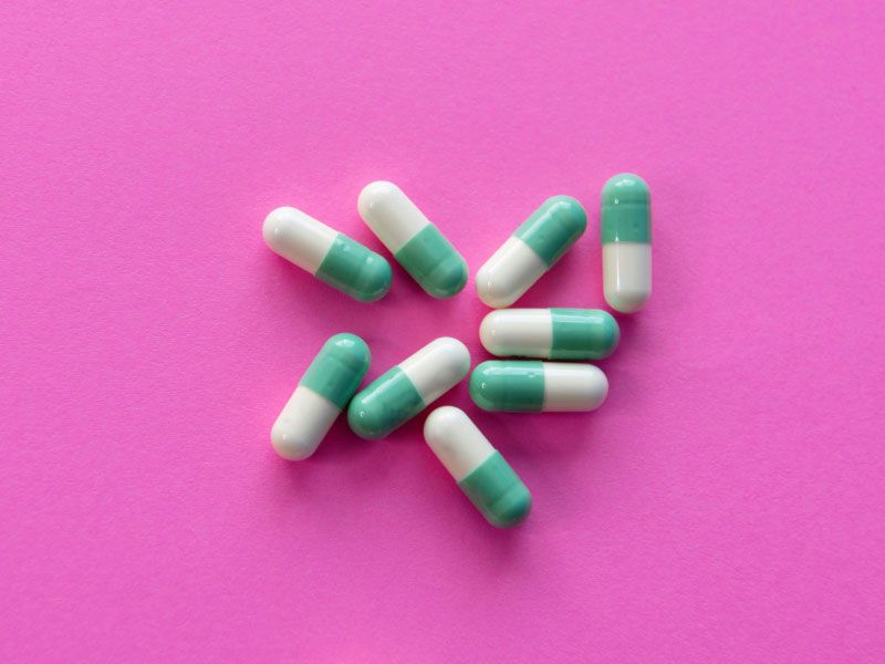 A group of white and green pills on a fuscia surface