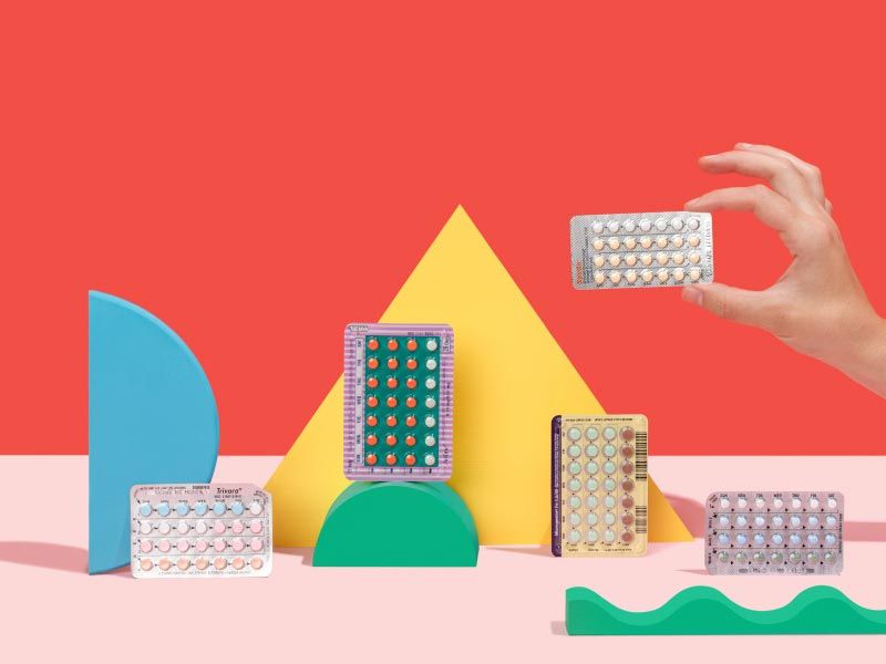 A woman's hand holding a birth control packet near 3 other birth control packets and multiple colorful geometric shapes on a red and pink background