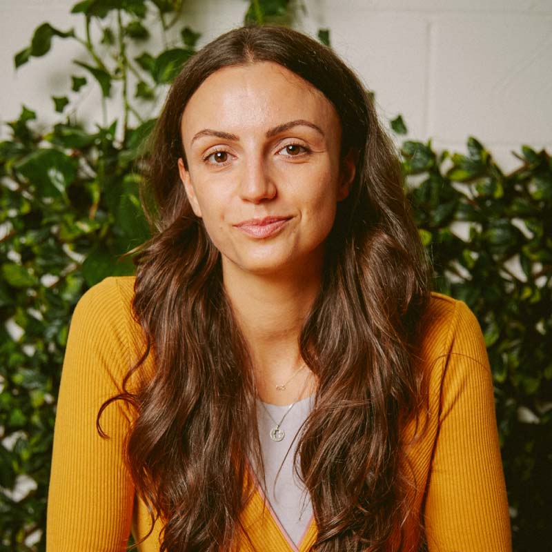 Valentina Milanova, founder of Daye, wearing a yellow sweater with greenery in the background