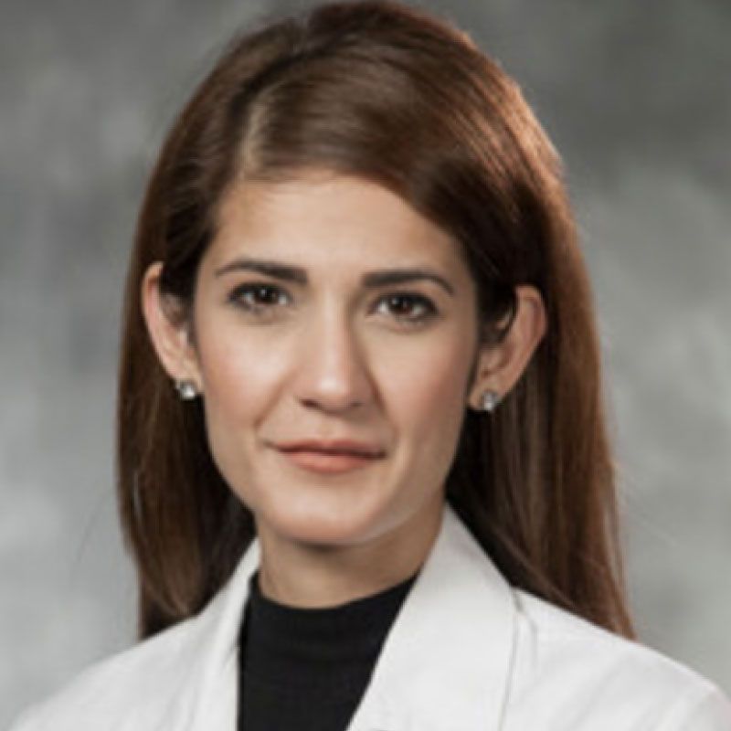 Dr. Meenal Kheterpal, MD, MMCi, FAAD wearing a white lab coat in front of a gray background