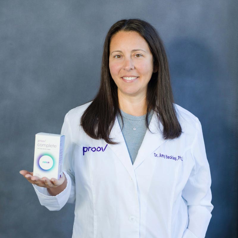 Dr. Amy Beckley, PhD wearing a lab coat and holding a Proov Complete box