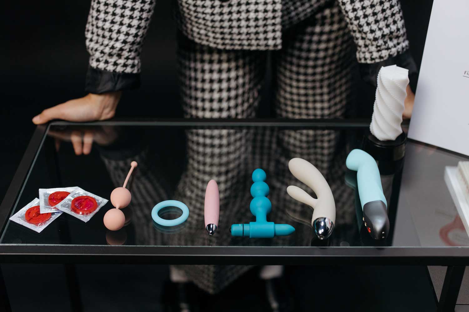 A person leaning on a table with several sex toys and condoms on the table