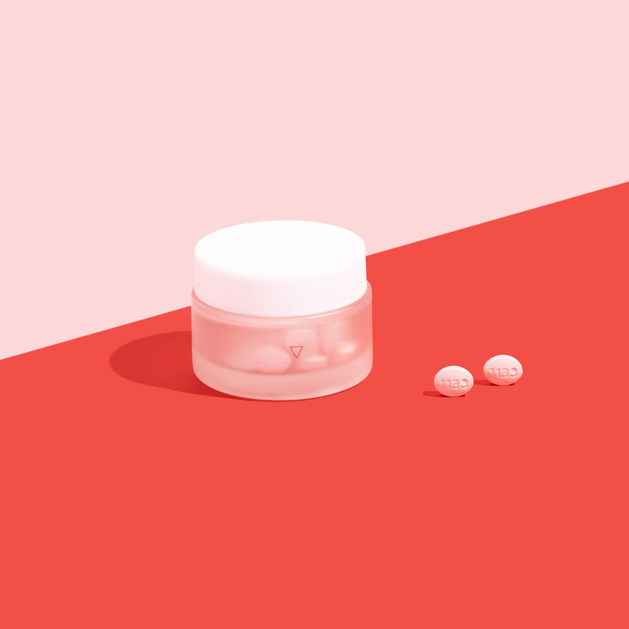 A glass jar of antifungals to treat yeast infections on a pink background and red surface