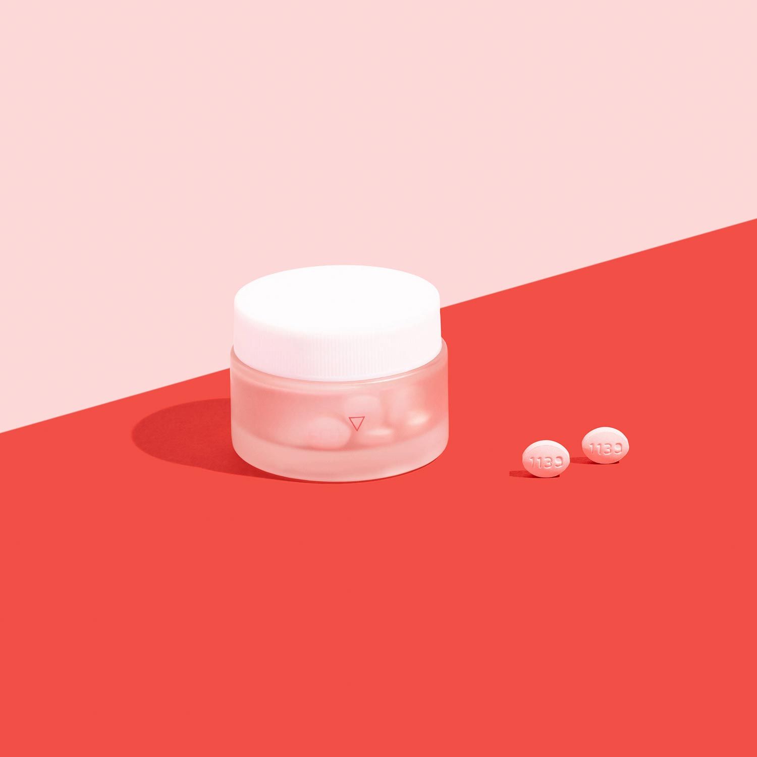A glass jar of antifungals to treat yeast infections on a pink background and red surface