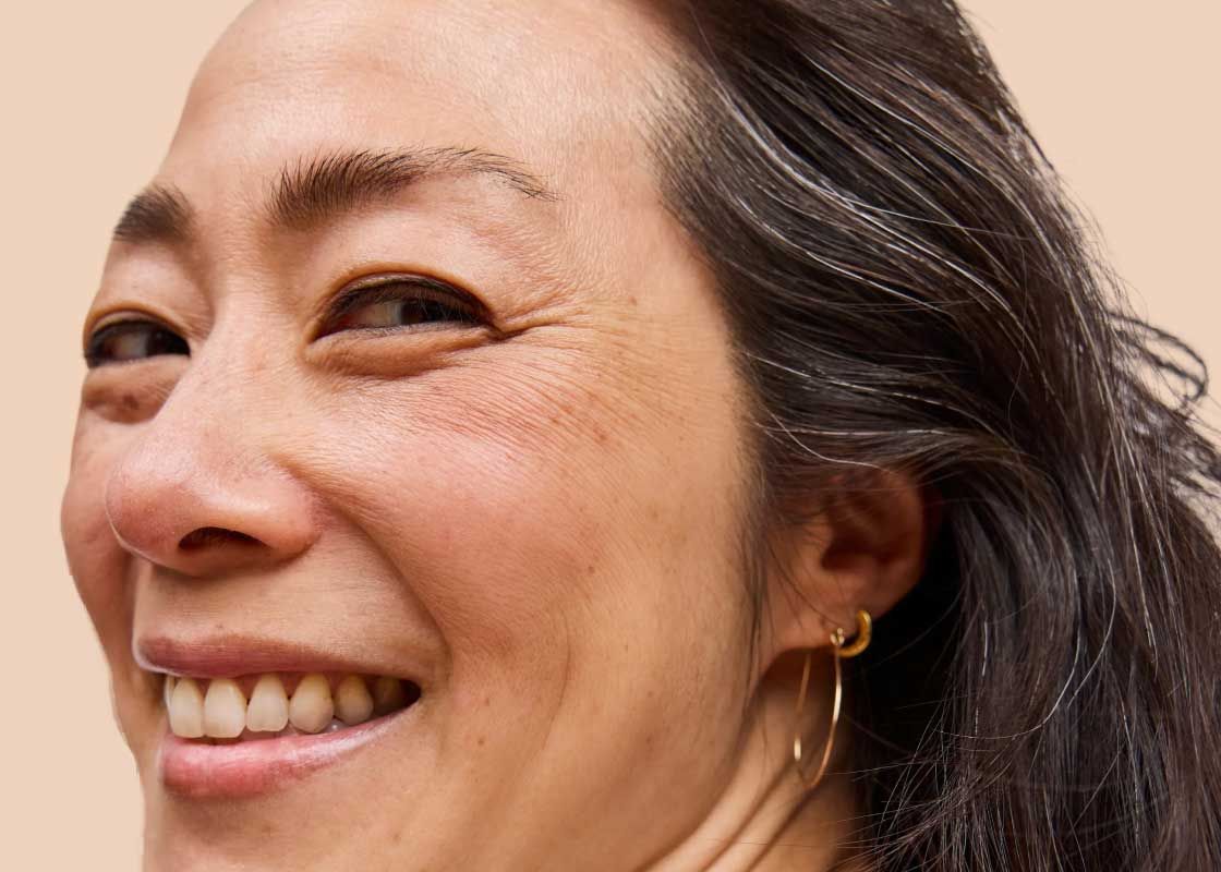 A close up of a smiling woman's face with a cream background