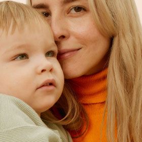 A blonde woman wearing an orange turtleneck holding her son
