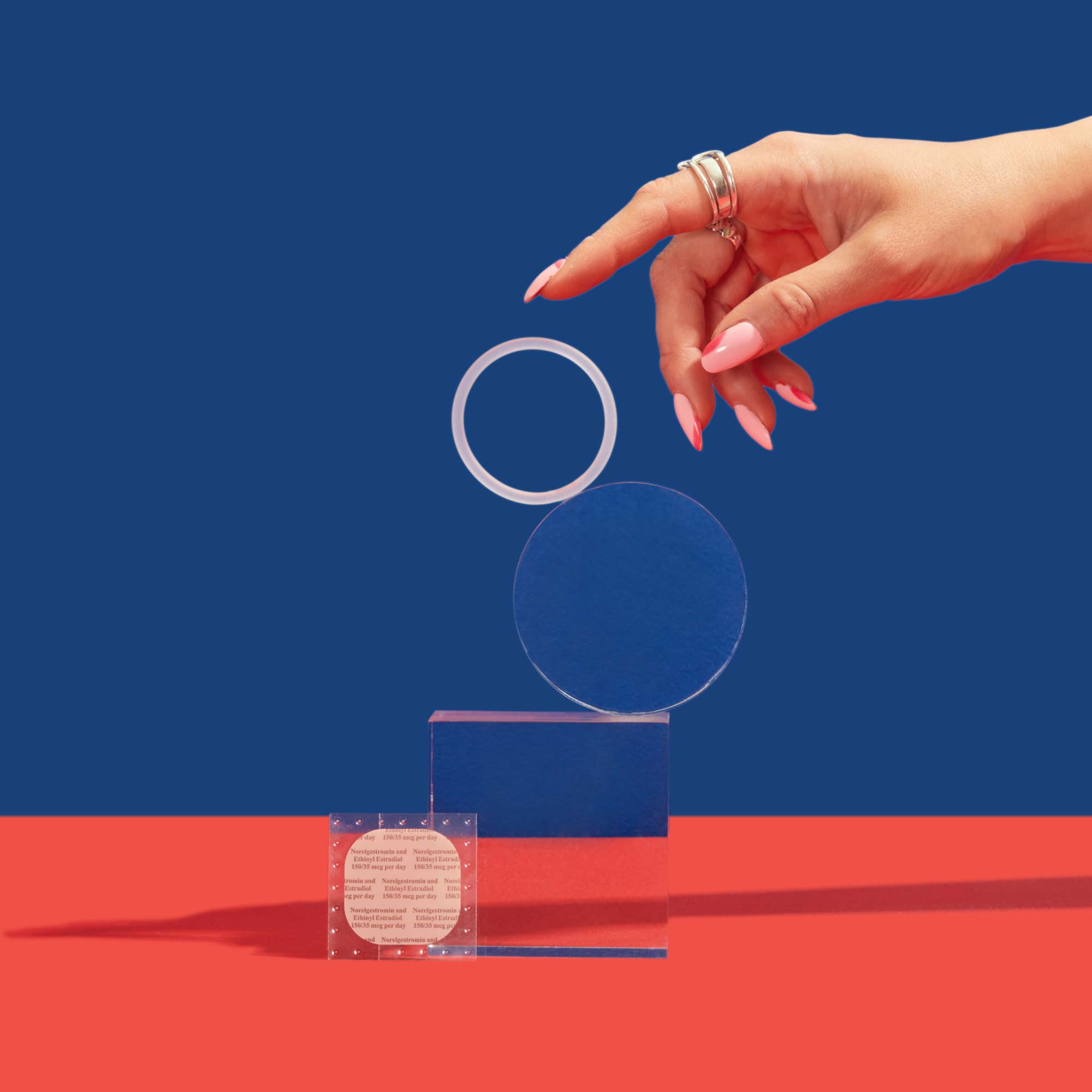 A woman's hand reaching for NuvaRing balanced on clear abstract shapes with the birth control patch on a red surface with a blue background