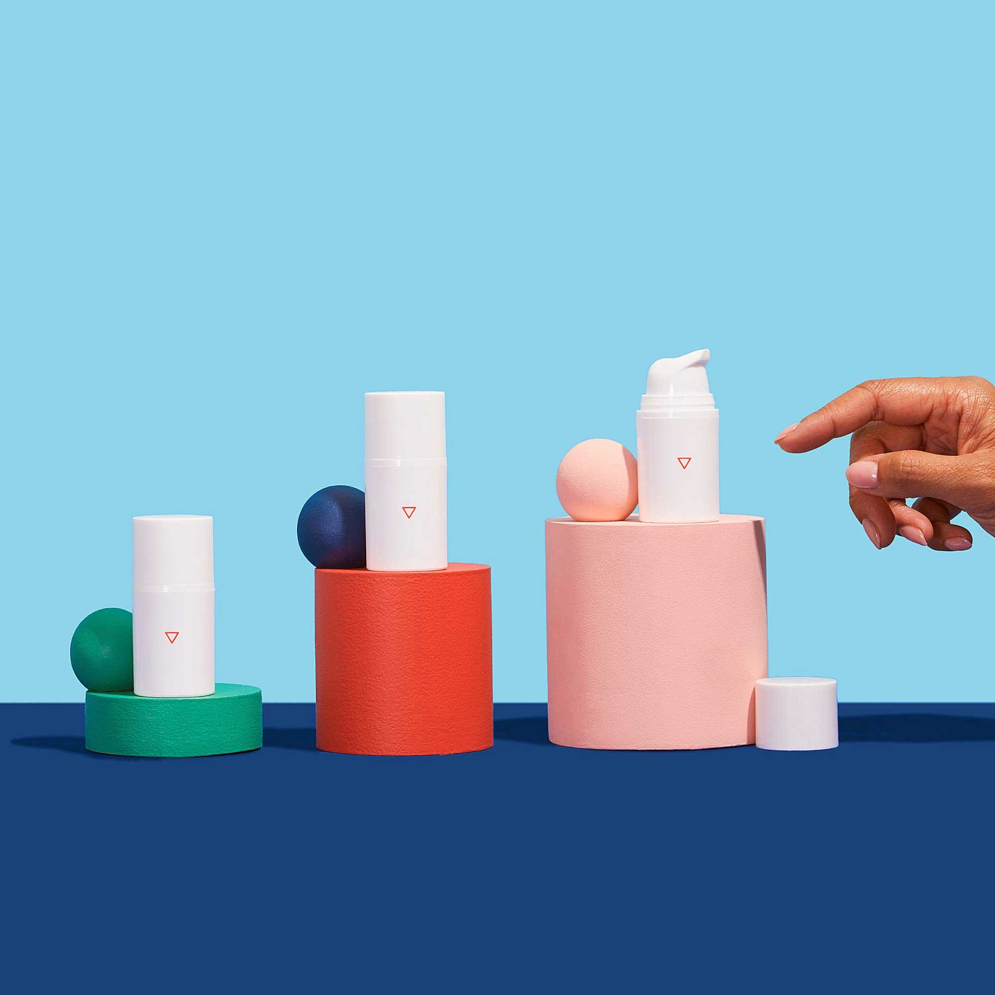 A woman's hand reaching for Wisp Calm Down Itch Cream bottles balanced on colorful abstract shapes on a dark blue surface with a light blue background