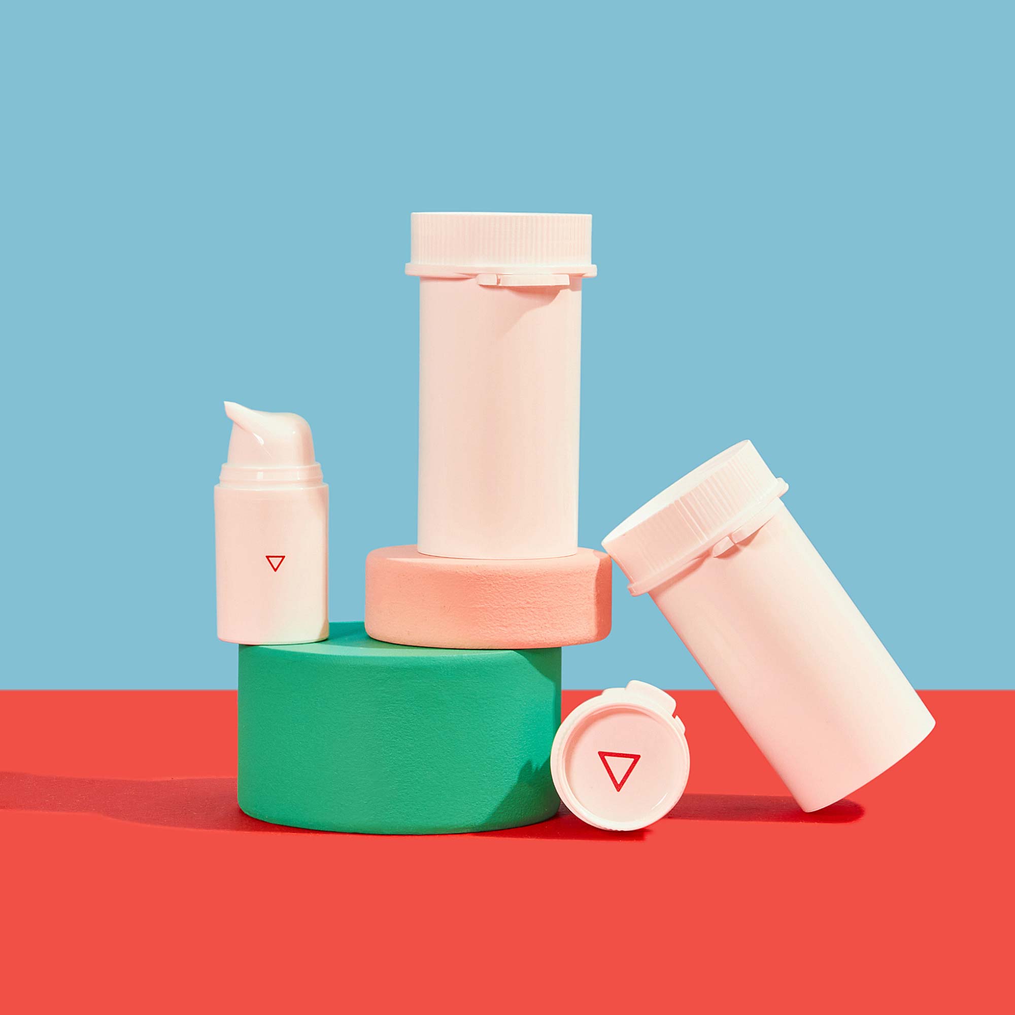 Wisp pill vials and pump bottles balanced on colorful abstract shapes on a red surface with a light blue background