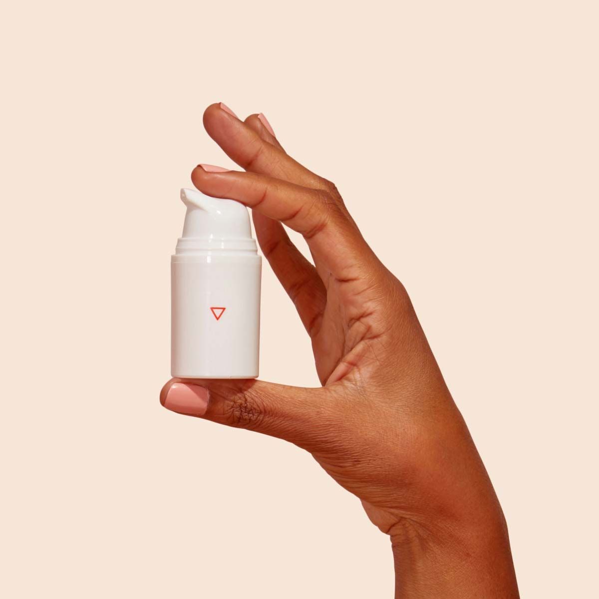 A woman's hand holding a pump bottle with a cream background