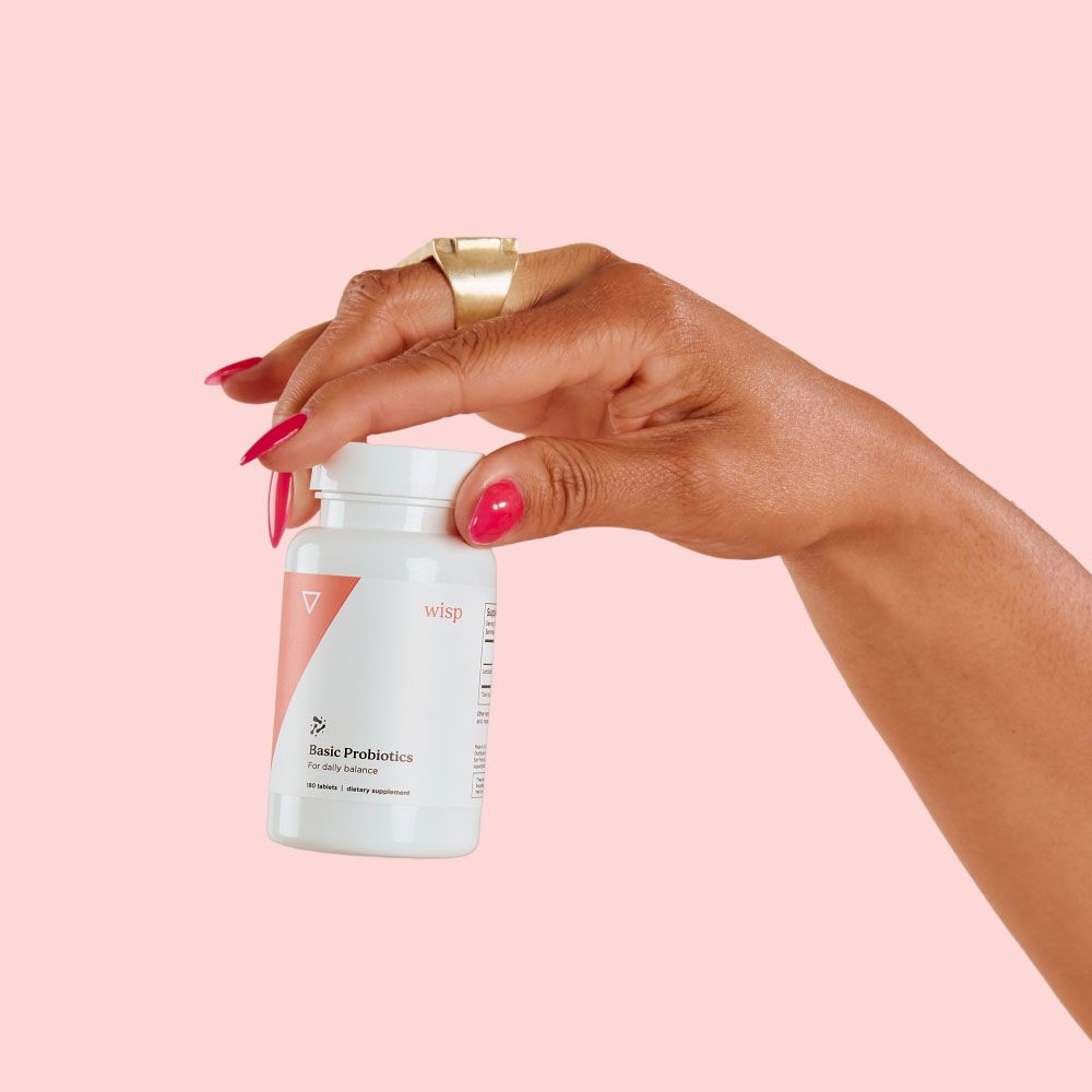 A woman's hand holding a bottle of Wisp Basic Probiotics in front of a pink background