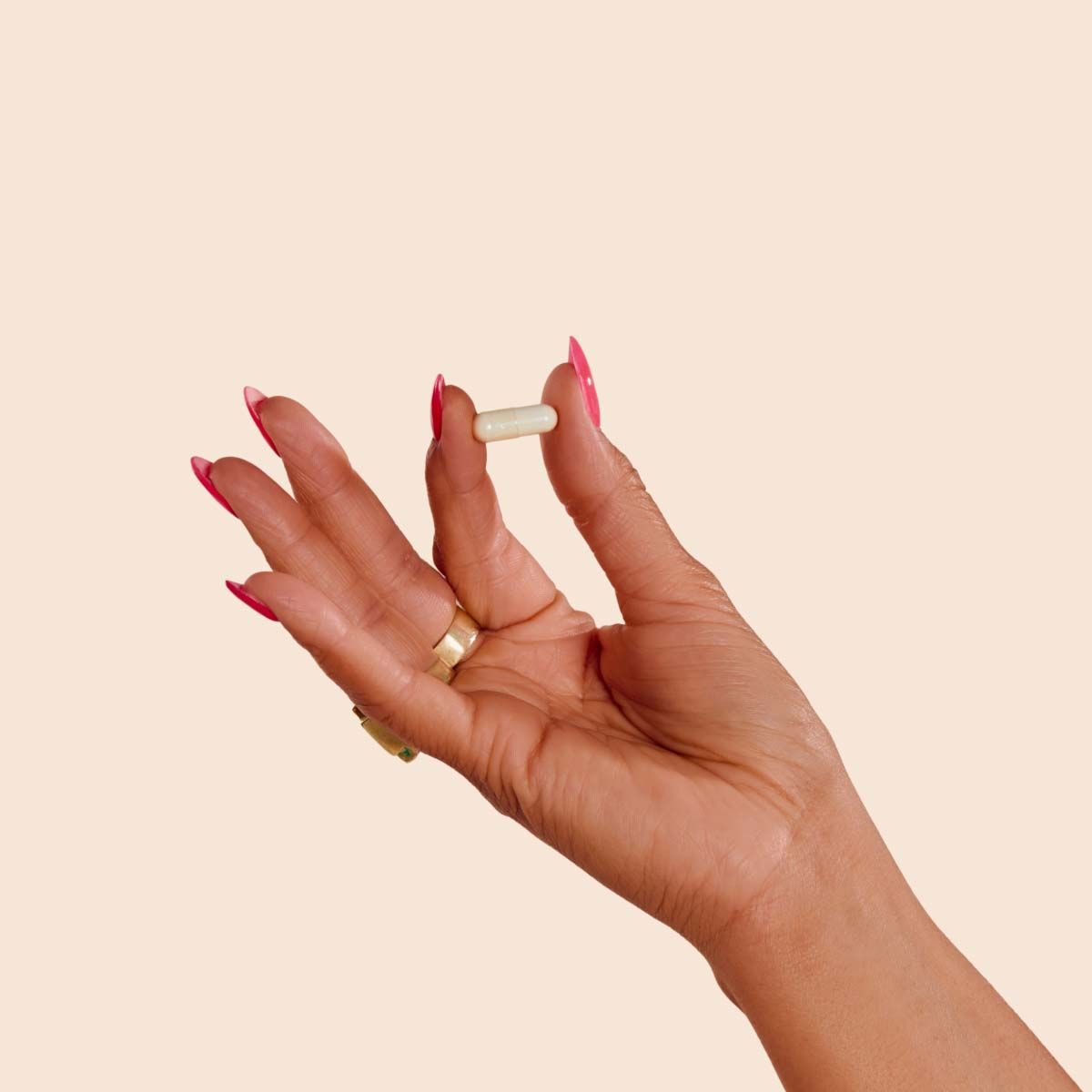 A close up of a woman's hand holding a Boric Acid Suppository in front of a cream background