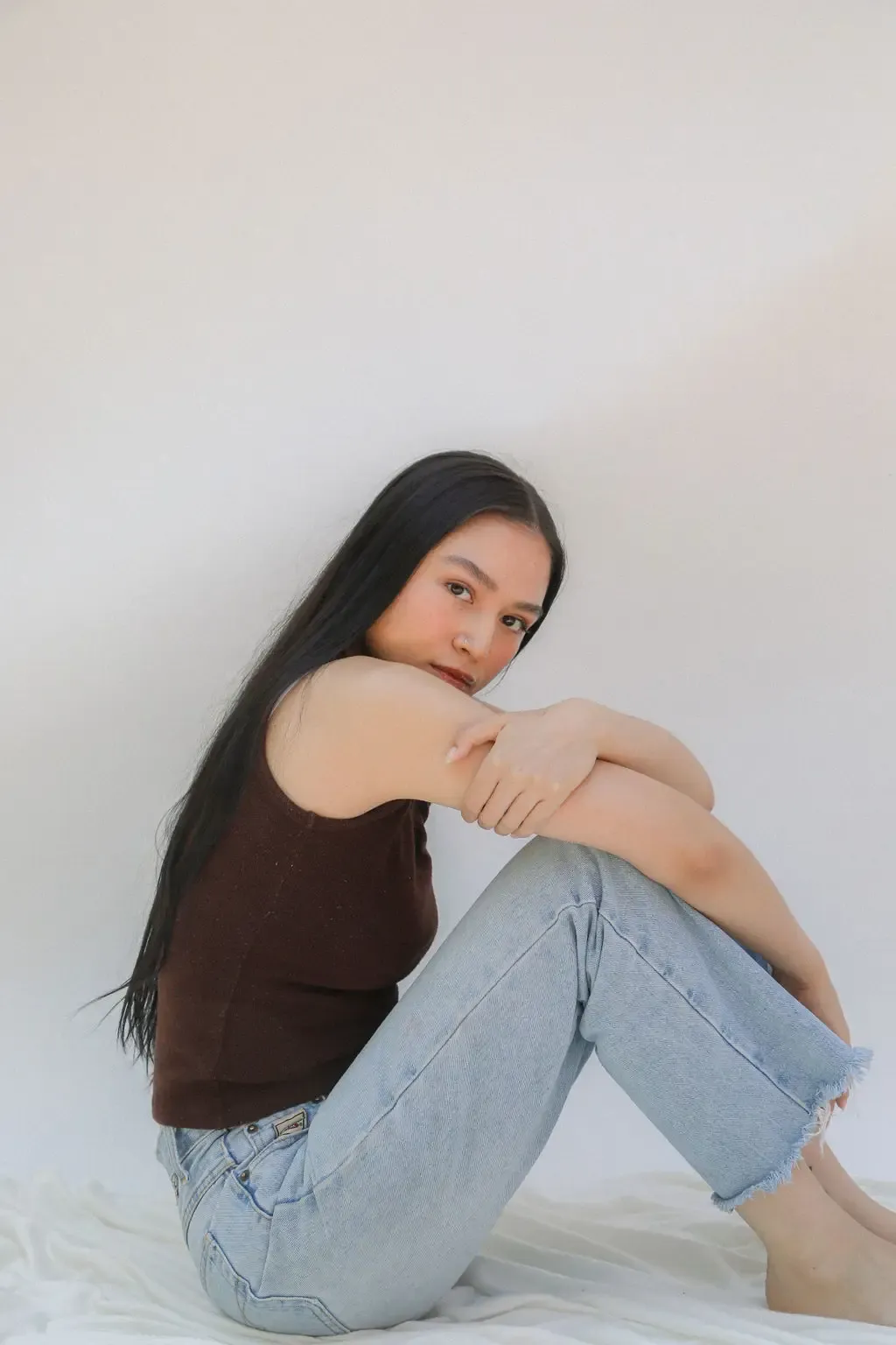 woman seated, wearing a black tank top and jeans