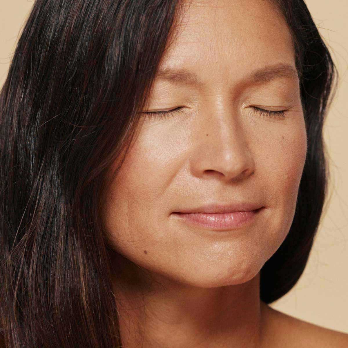 A pleasant looking woman with dark hair and a cream background
