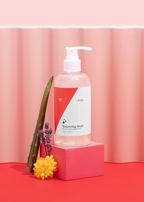 Wisp Balancing Wash on a pink block with dandelion, aloe vera, and lavender with colorful abstract shapes on a red surface with a pink background