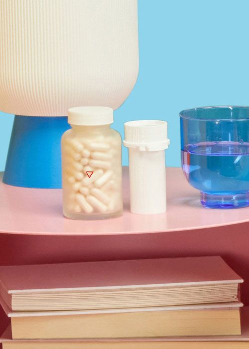 A tall Wisp pill jar and a plastic vial on a pink nightstand with a blue glass of water and a lamp