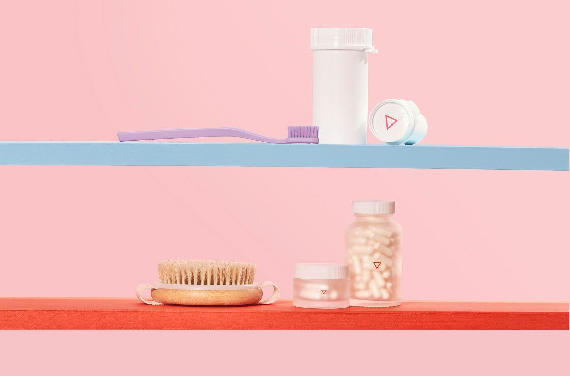 Wisp plastic vials and glass pill jars on colorful shelves with a purple toothbrush and a dry brush in front of a pink background
