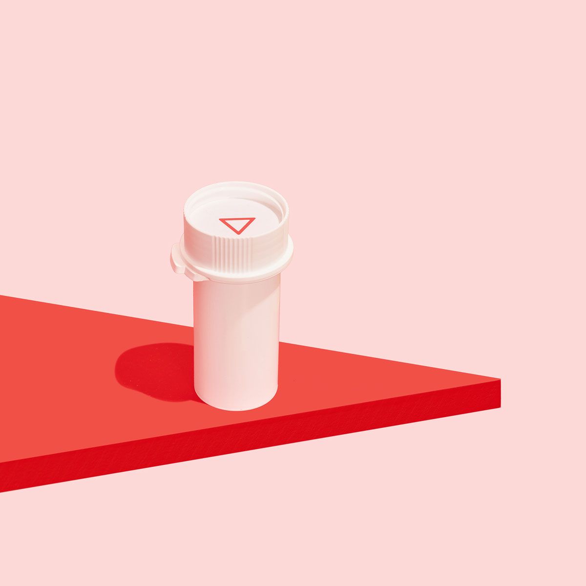 A white pill vial on a red surface with a pink background