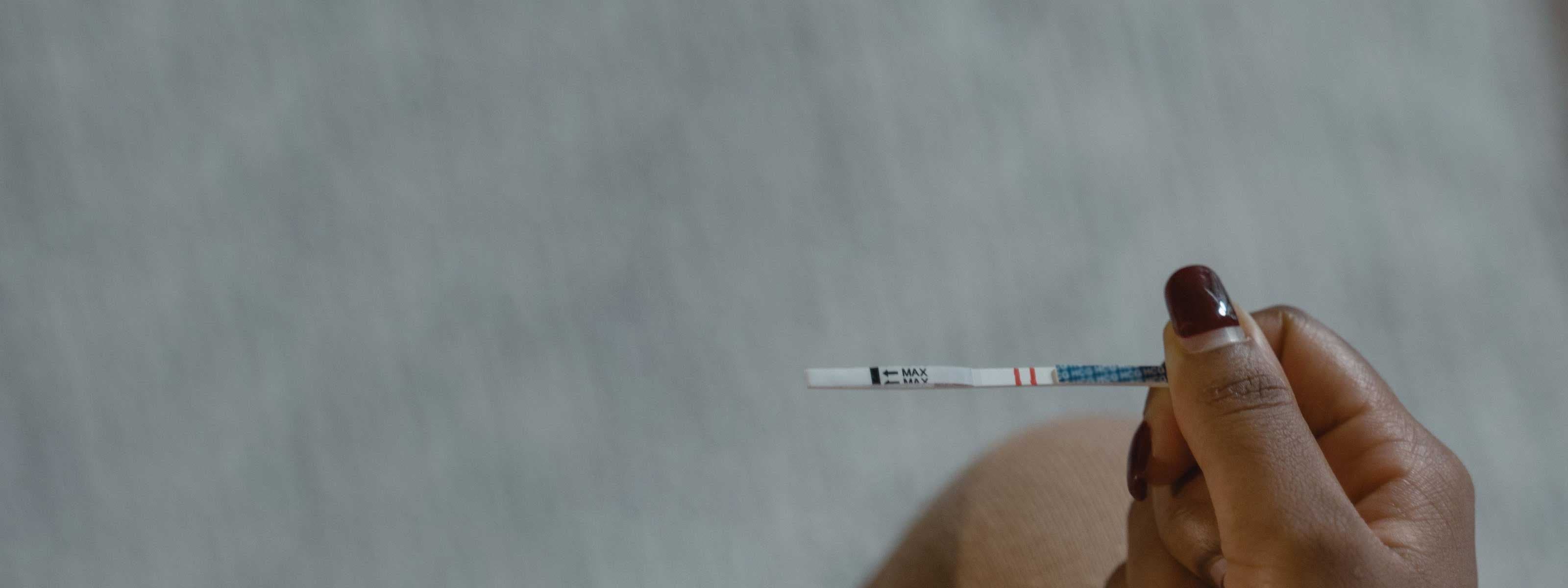 A woman's hand with painted nails holding a testing strip with an ambient background