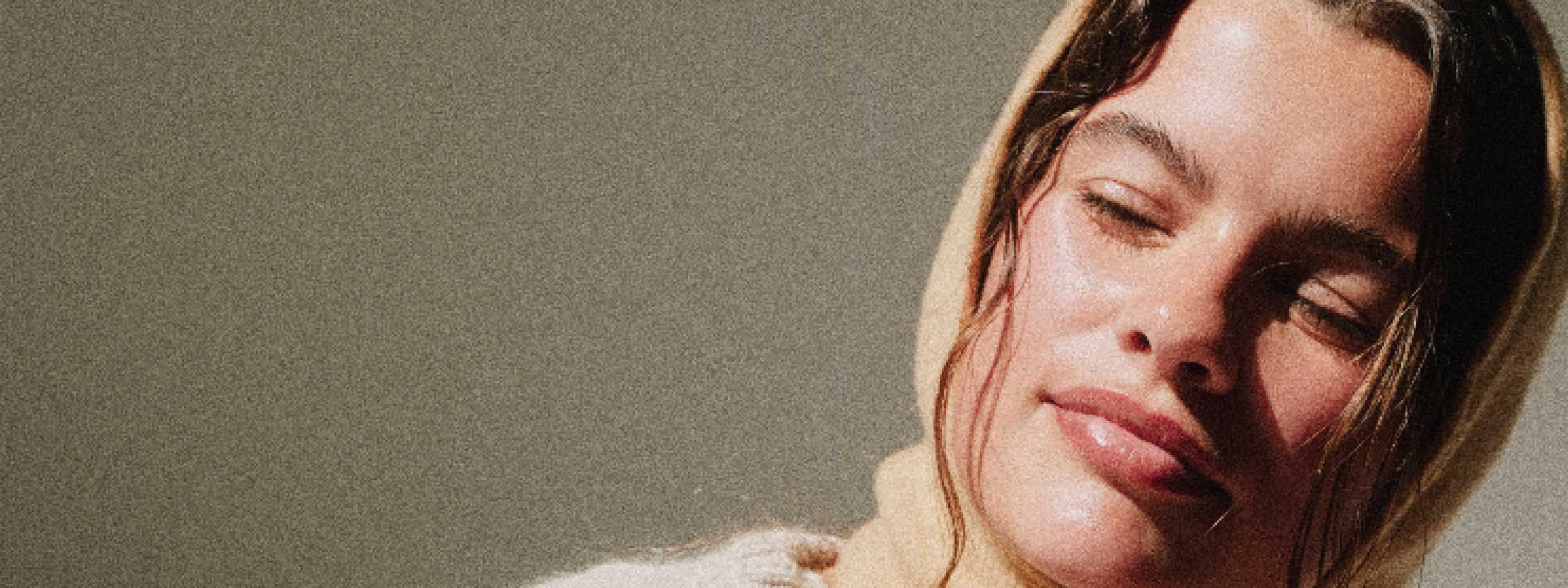 A smiling woman with brown hair and a gray sweater with glowing skin