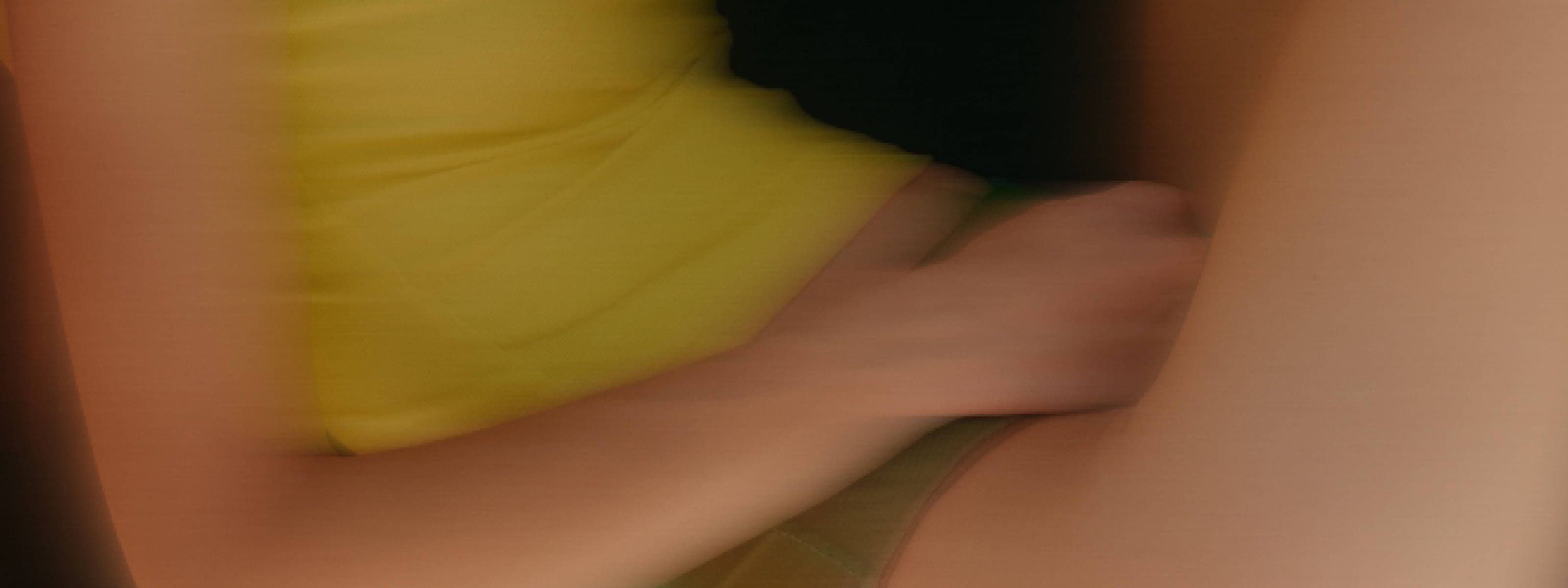 Blurred close-up photo of a person's arm and hand pressed against their abdomen, conveying a sense of pain or discomfort