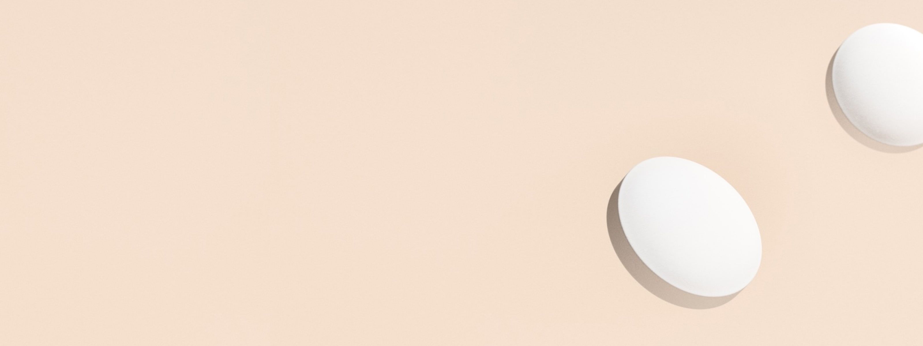 image of two white pills in front of a beige background
