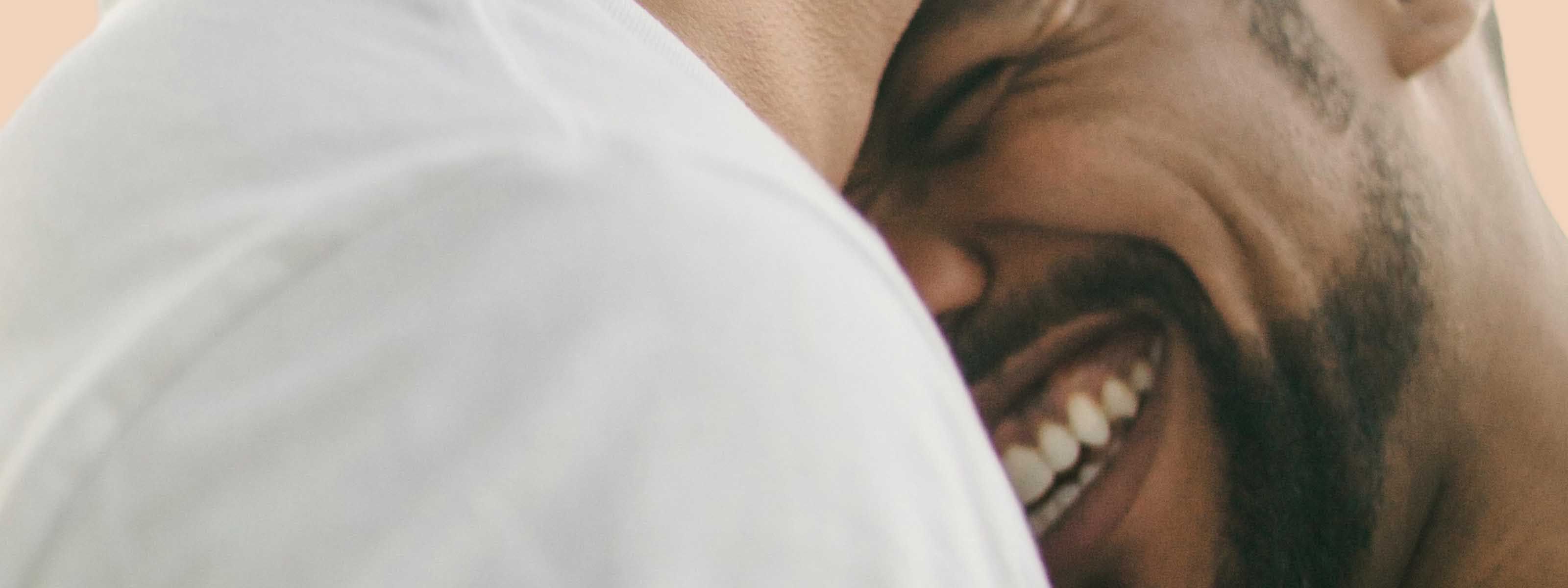 Close-up of a smiling person partially hidden behind someone’s shoulder