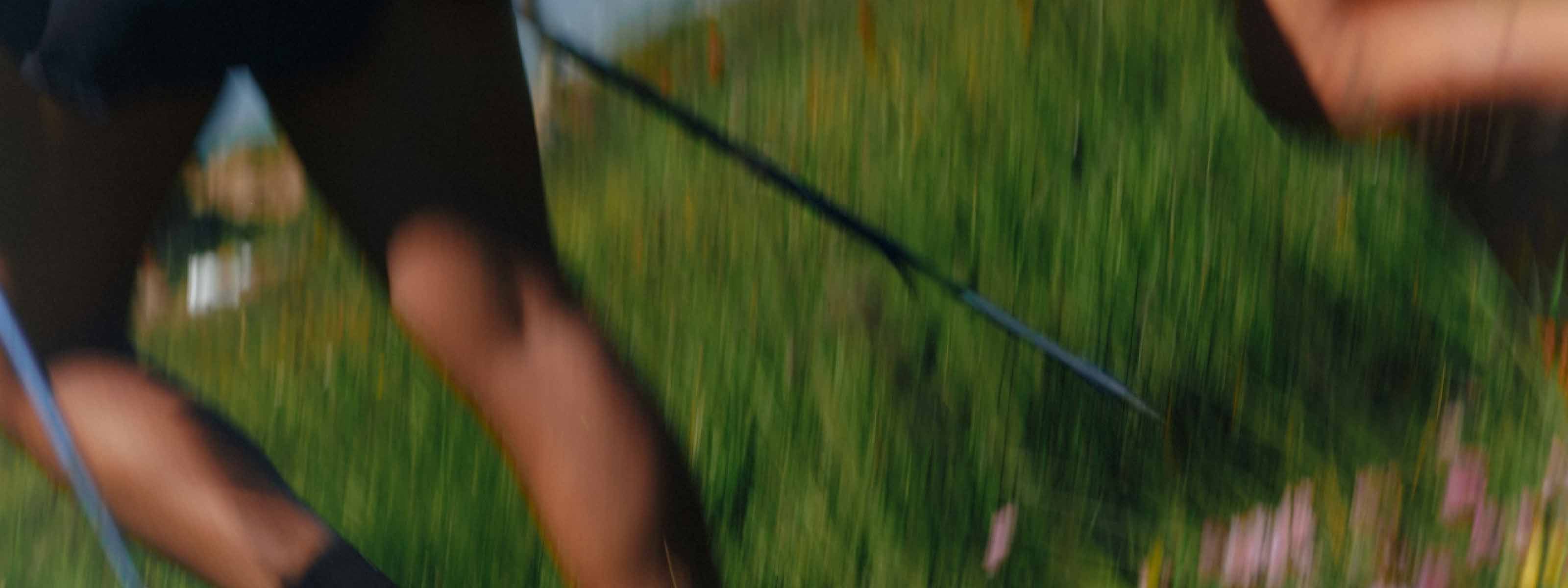 Blurred shot of legs moving through a green field with hiking pole in hand.