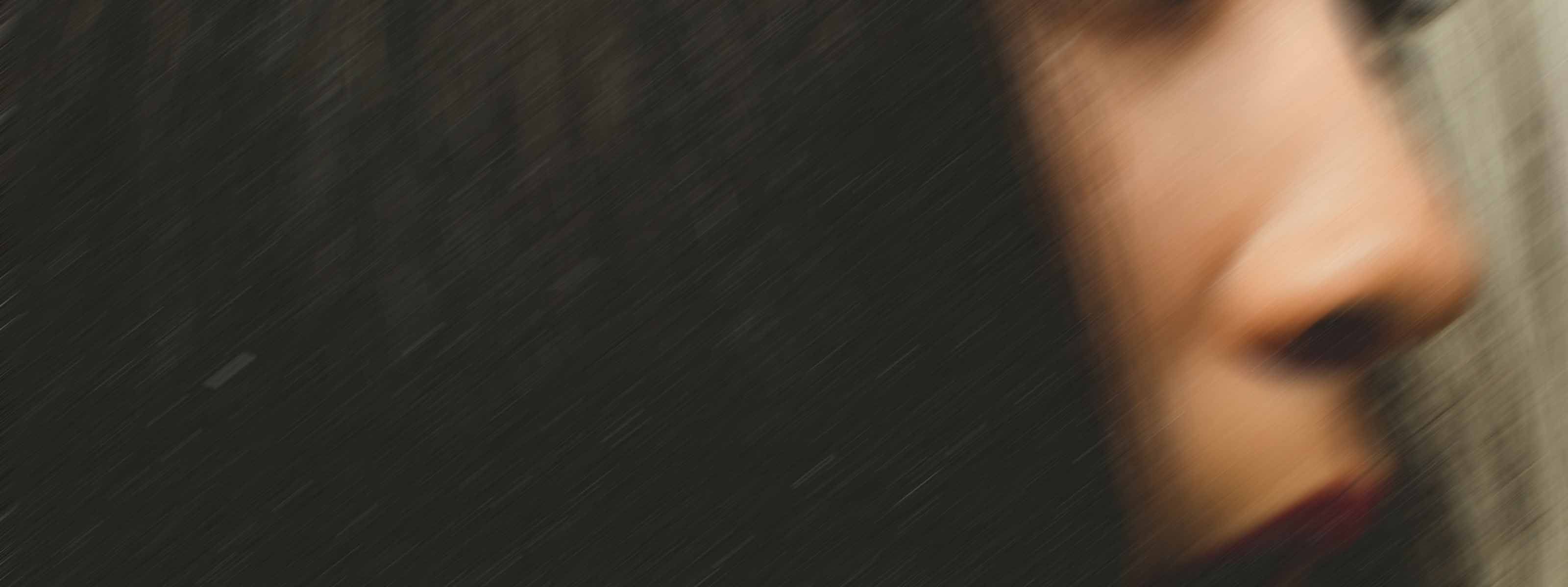 Soft-focus profile of a person's nose and lips against dark hair in low light.