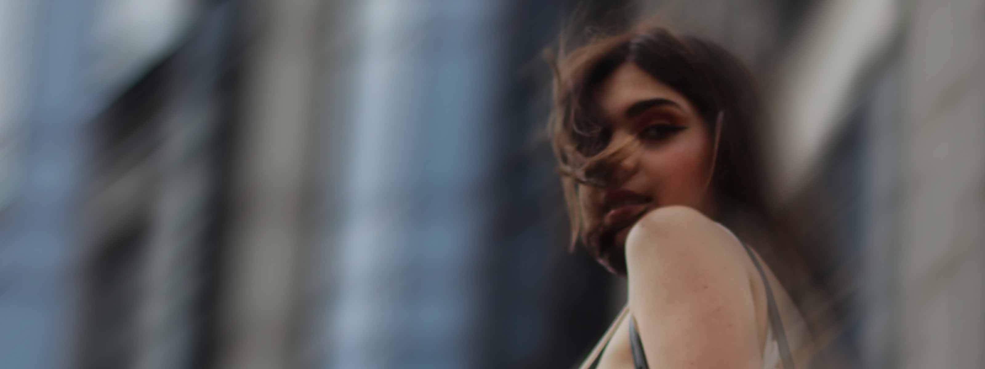 Woman with windswept hair looking over her shoulder in front of a blurred city building.