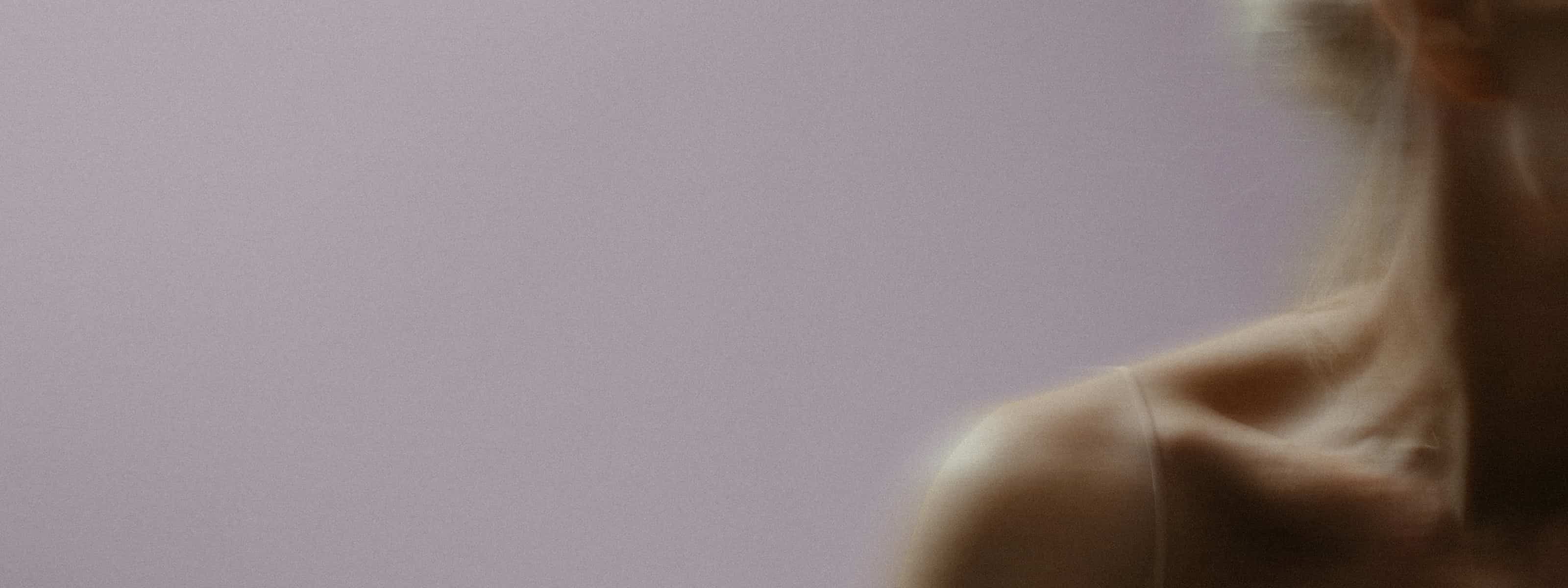A softly blurred close-up of a person's shoulder and neck area against a muted background.