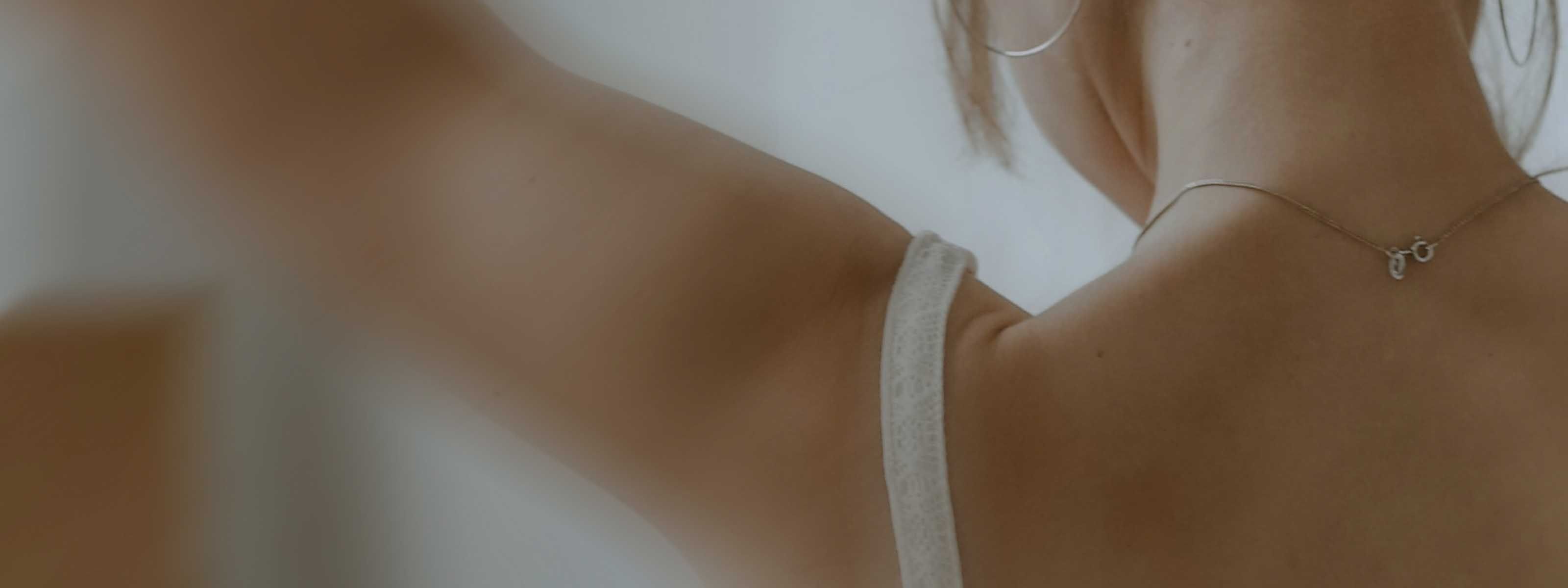 Close up of the back of someone raising their arms while wearing a white top
