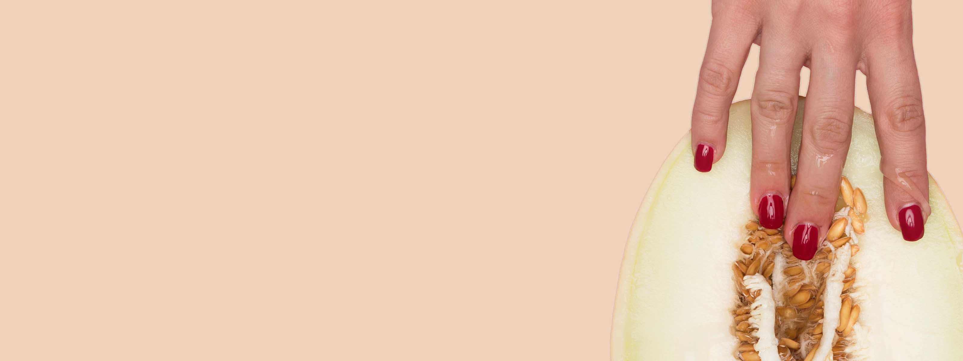 Hand with red nail polish touching the seeds of a sliced melon against a plain background.