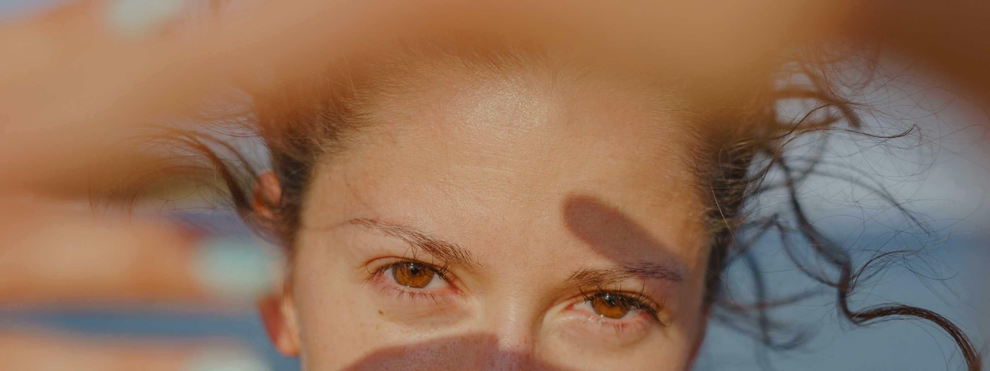 Close-up portrait of a woman with wet hair and warm brown eyes in natural sunlight.