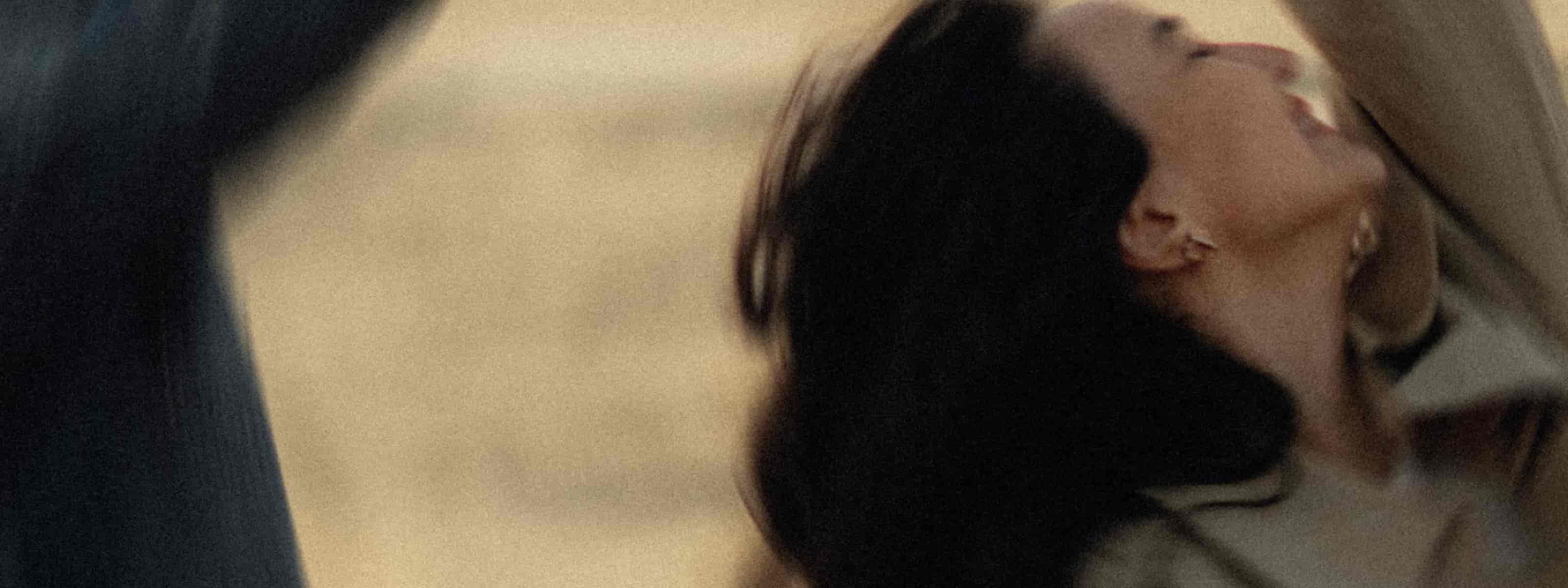 A woman with dark hair tilting her head back, captured in a cinematic, warm-toned close-up.