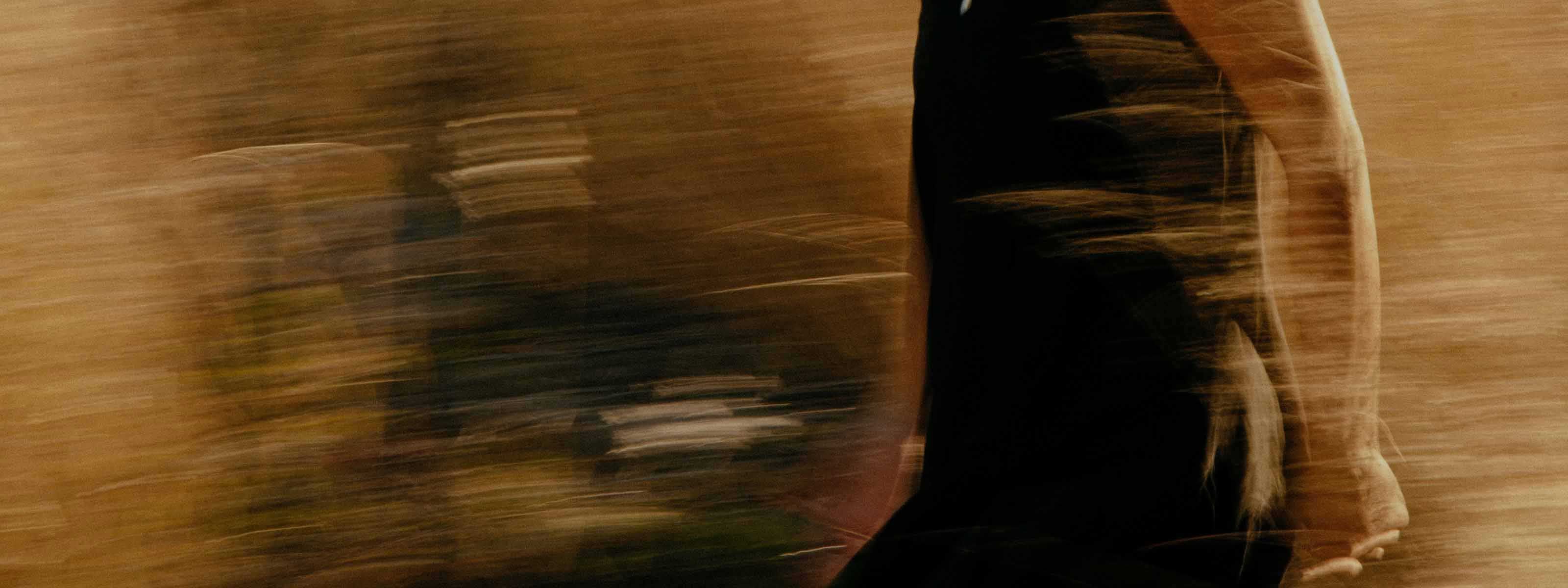 Motion-blurred torso of a person in a black top against a warm golden background.