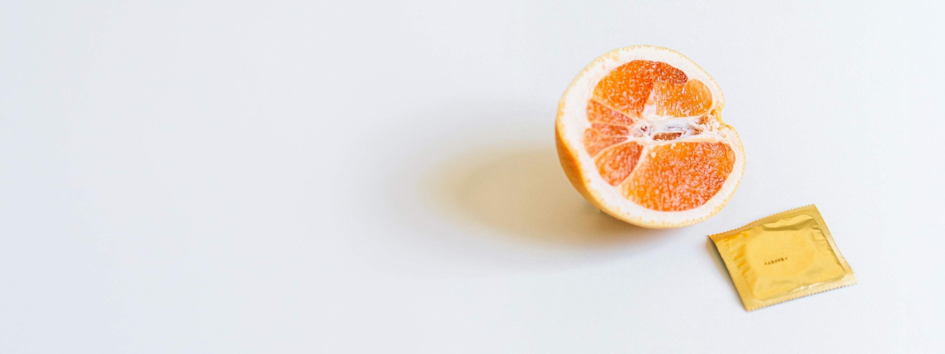 a white background with half an orange facing outwards next to a gold foil square packet