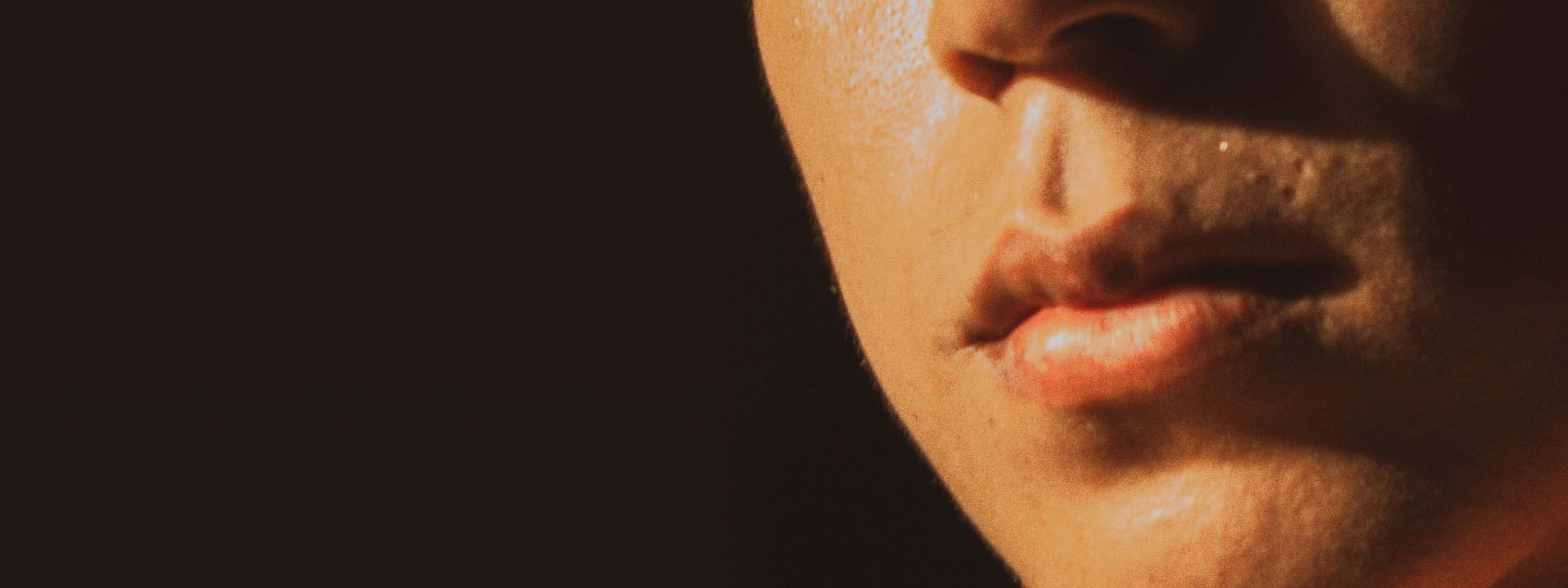 Close-up of a person’s lower face, lit by warm light against a dark background.