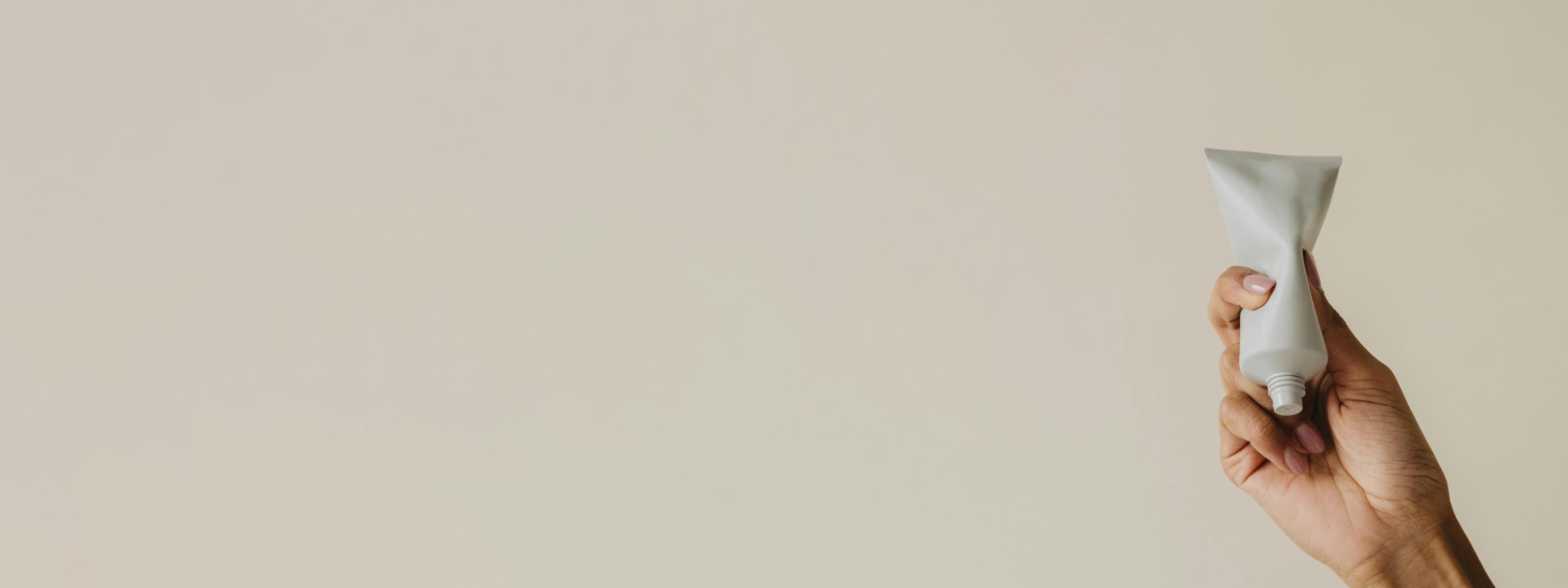 A person's hand holding a white tube in front of a beige background