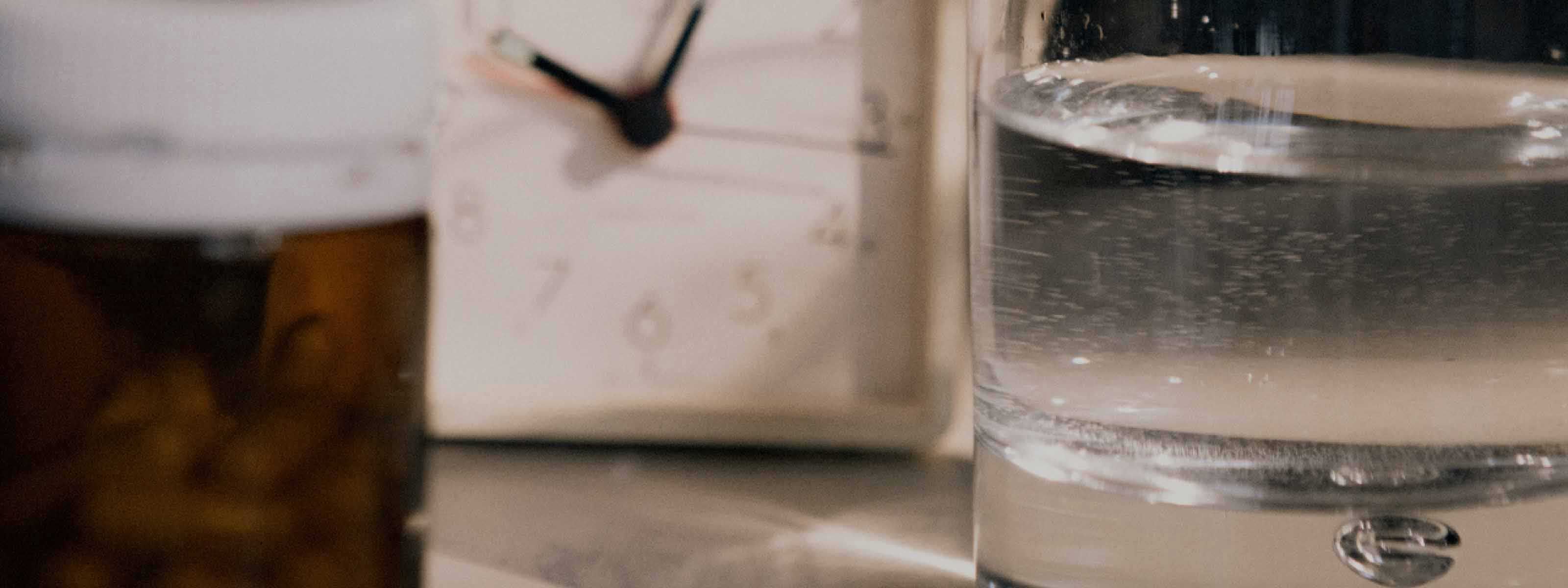 An amber pill vial, alarm clock, and glass of water on a nightstand