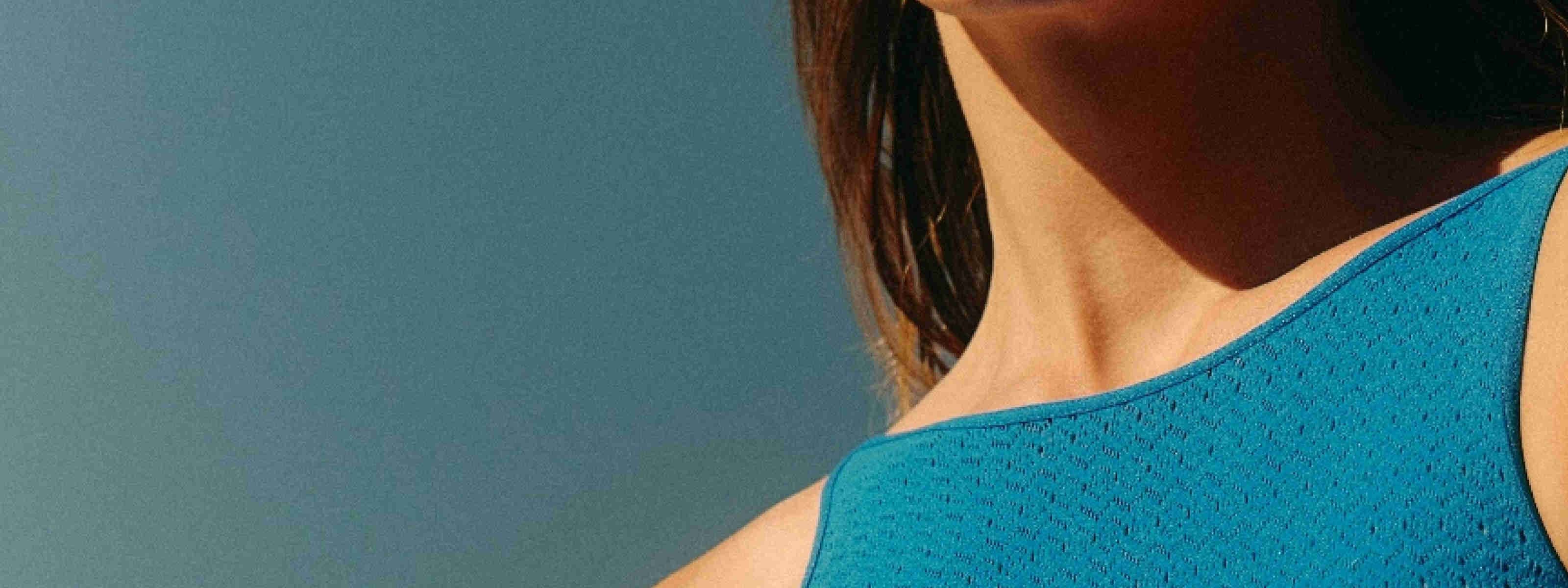 Close-up profile view of a woman's neck, showing the throat area, against a teal background.