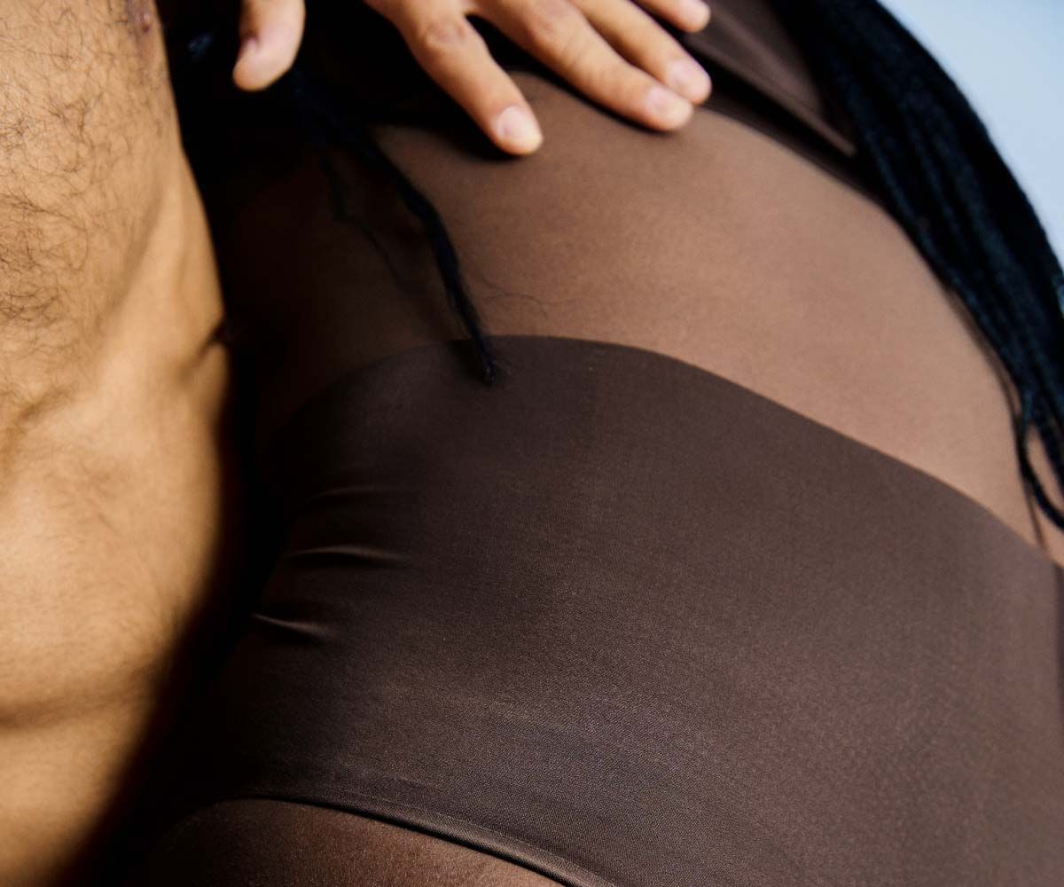 An abstract crop of a woman wearing brown underwear with a light blue background
