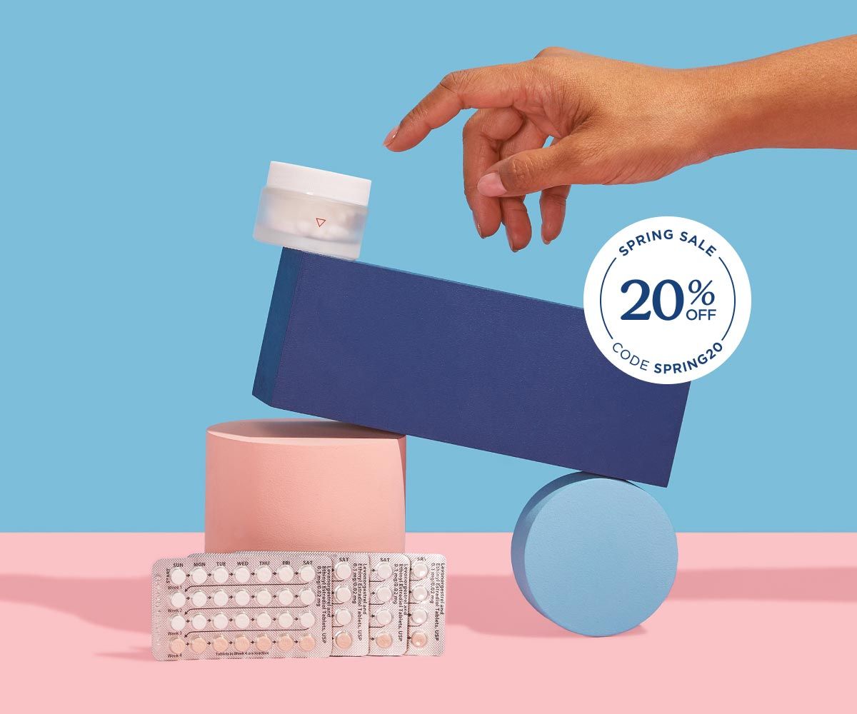 A Wisp glass pill jar and multiple birth control packets balanced on colorful abstract shapes on a pink surface with a light blue background